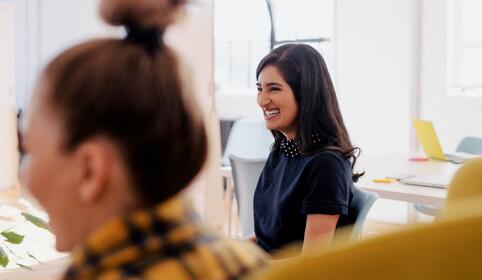 To smilende damer sitter i et kontorlokale