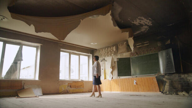 Kvinne står midt i et klasserom ødelagt etter russiske angrep