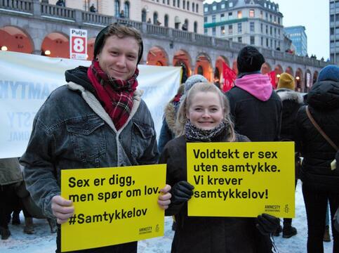 Mann og kvinne står med plakater under 8. mars-markering. Plakatene sier "Sex er digg, men spør om lov. Samtykkelov nå!"